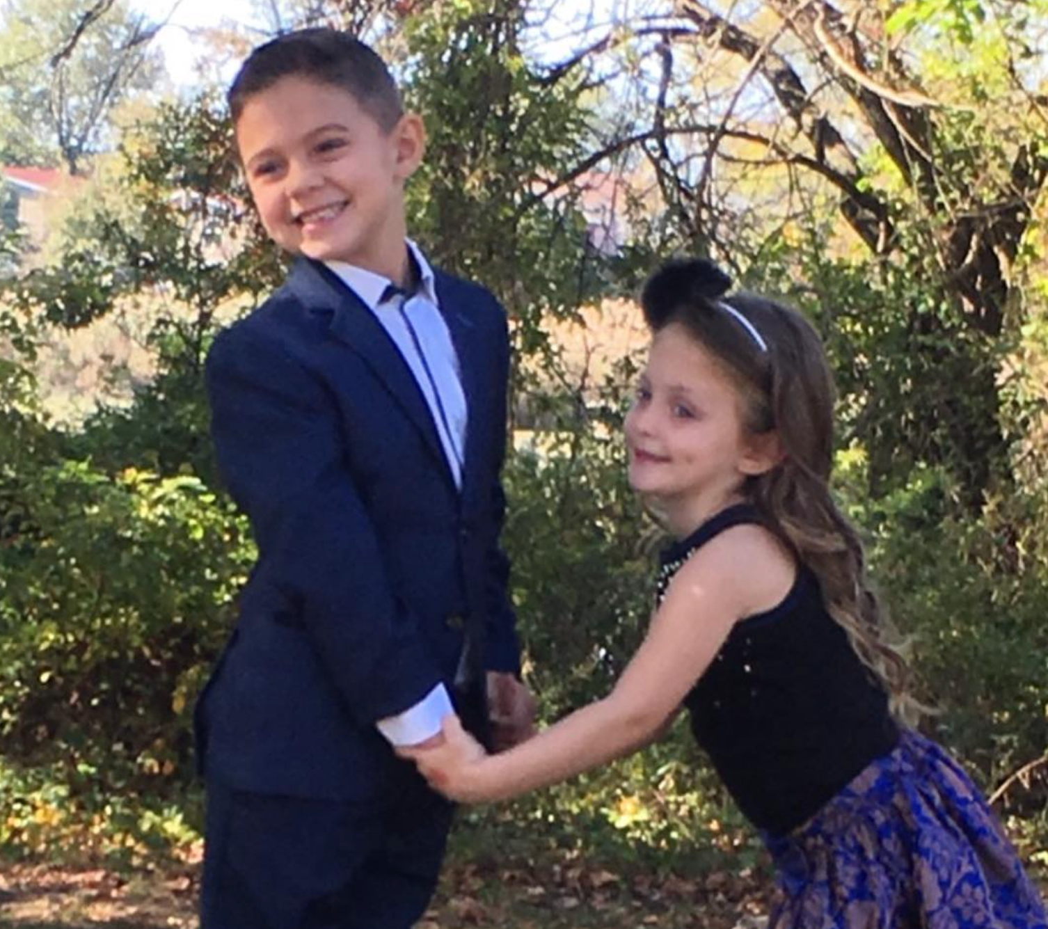 boy in a blue suit and white shirt, holding hands with girl in tank top and skirt