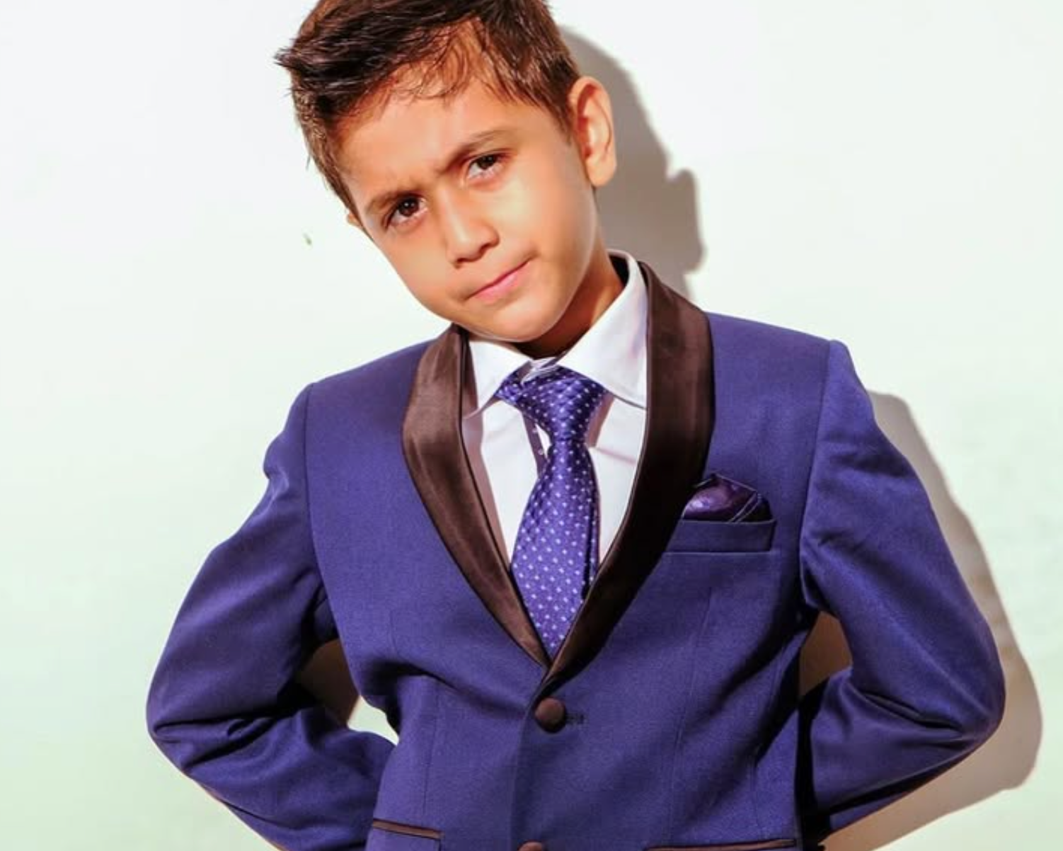 Young boy wearing a purple suit with a white shirt and blue tie on a light background