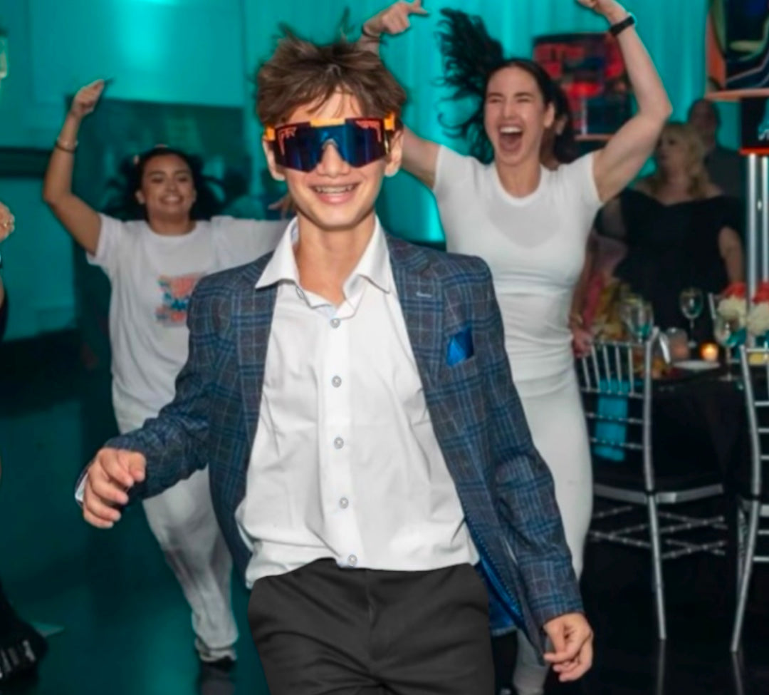 young boy at a party dancing while wearing white kids dress shirt, and blazer, and pants