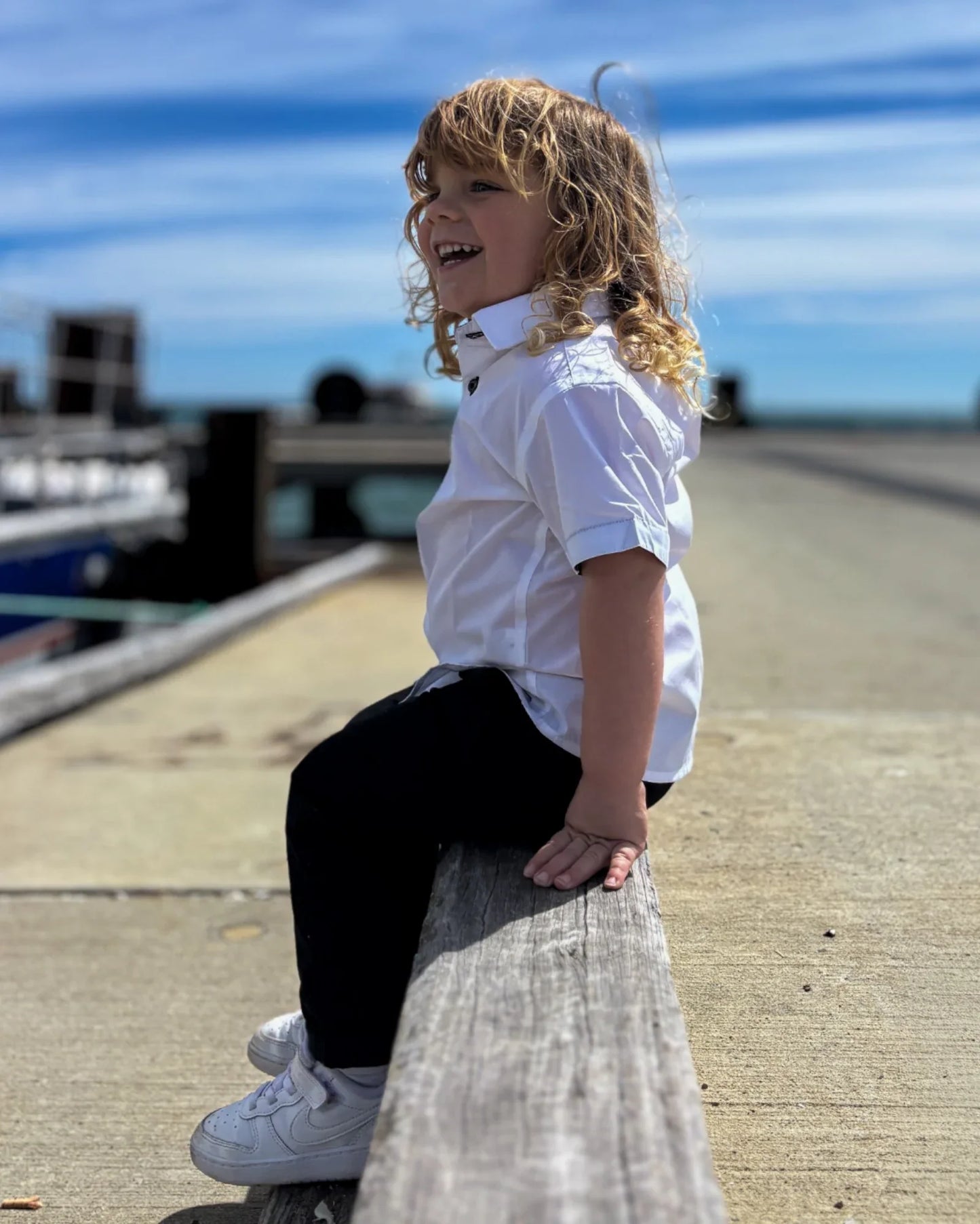 Boy wearing short sleeves shirt and chinos, sitting on a pier