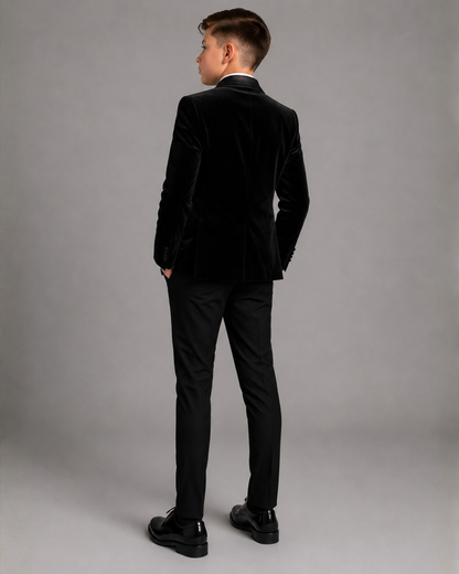 Boy wearing a black velvet suit against a Grey background back view