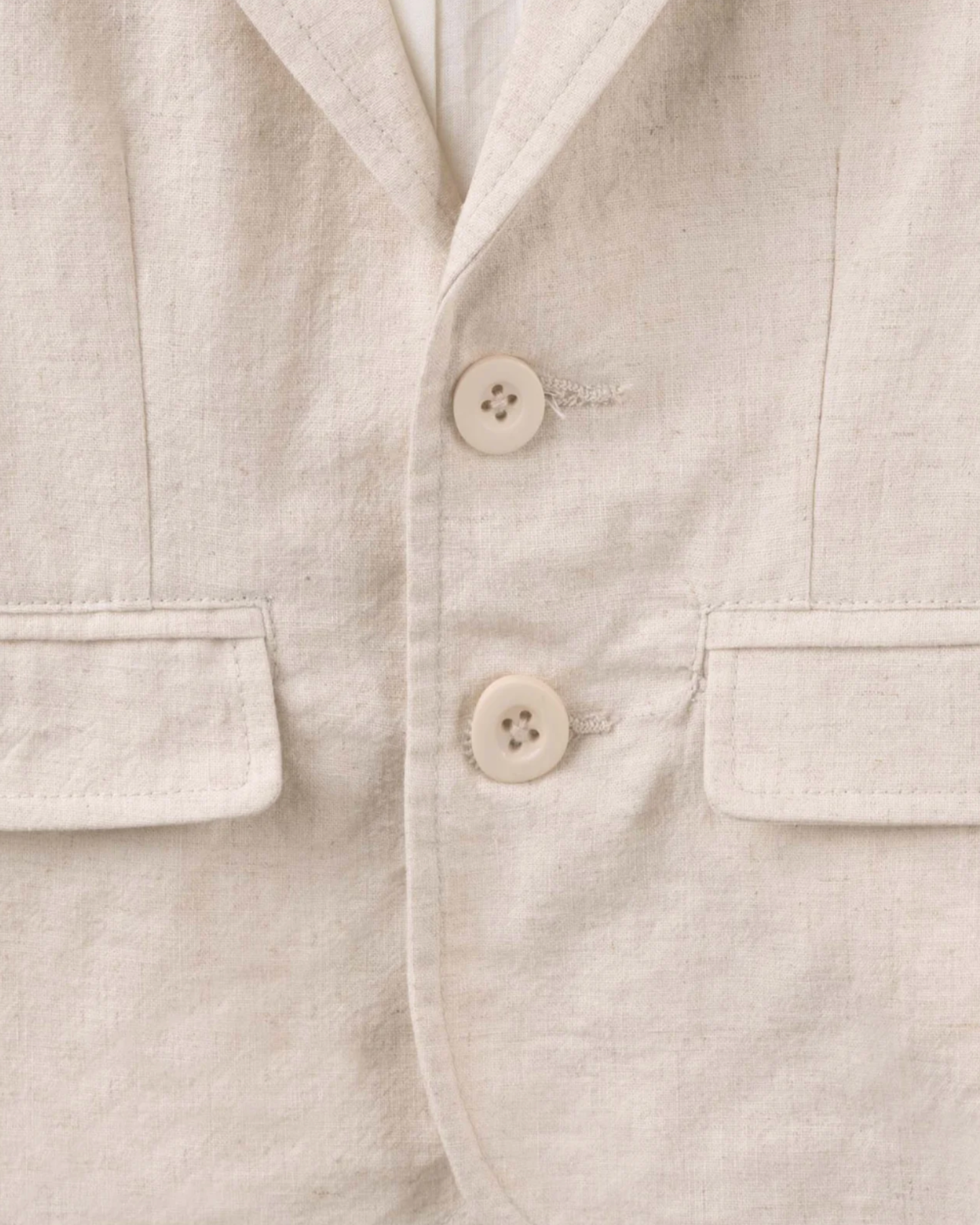 Close-up of a light beige linen jacket or shirt with two cream buttons and flap pockets.