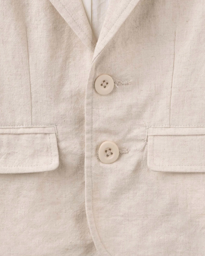Close-up of a light beige linen jacket or shirt with two cream buttons and flap pockets.