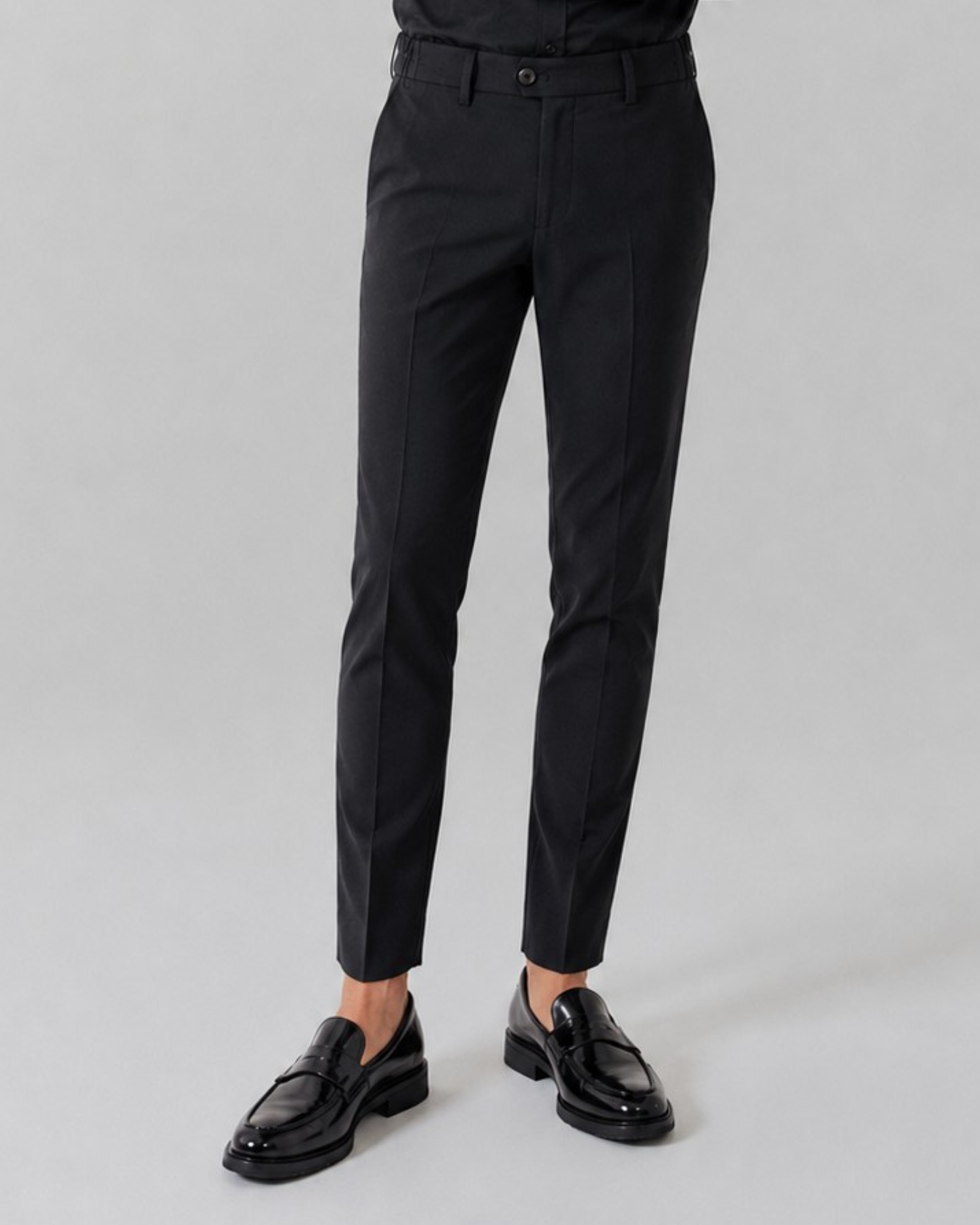 Black dress pants worn by a person on a gray background