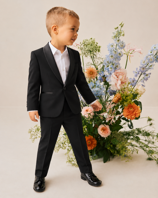 Boy in a black tuxedo wearing a white shirt, while standing