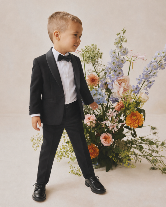 Young boy standing in a black tuxedo, wearing a white shirt and bow tie