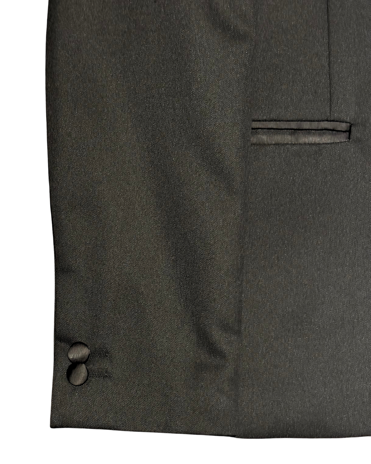 Close-up of a boys’ black tuxedo jacket showing the satin-trimmed side pocket, fabric texture and two satin-covered sleeve buttons.