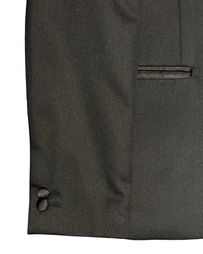 Close-up of a boys’ black tuxedo jacket showing the satin-trimmed side pocket, fabric texture and two satin-covered sleeve buttons.