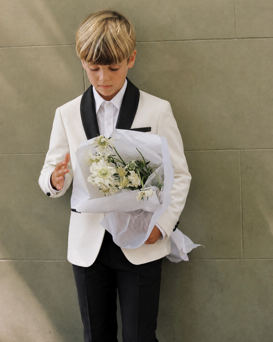 Young boy in a white velvet blazer and white shirt and black dress pants, holding a bouquet of flowers 