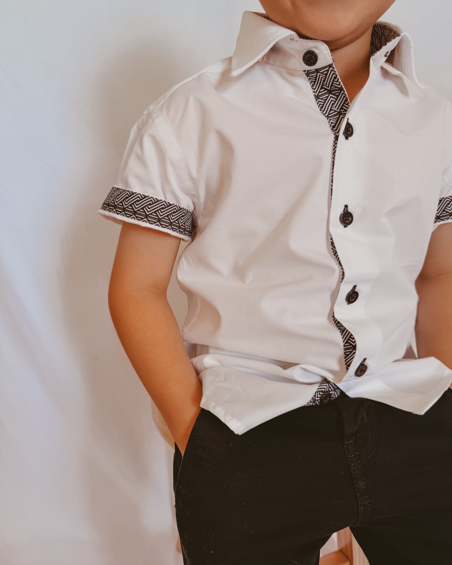 Child wearing a white shirt with black patterns on a plain background