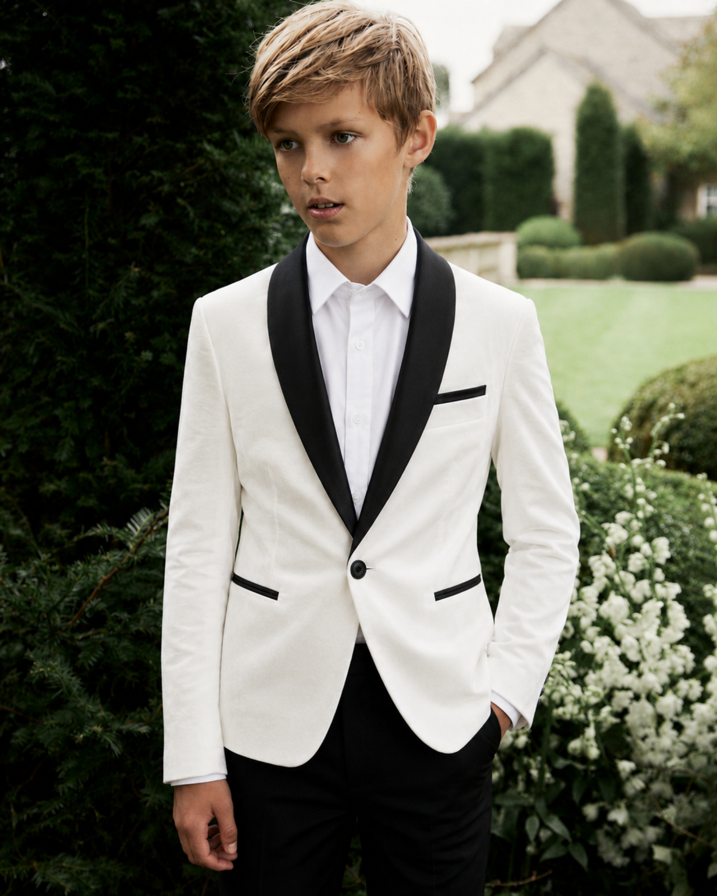 Young boy in a white suit with black lapels standing outdoors.