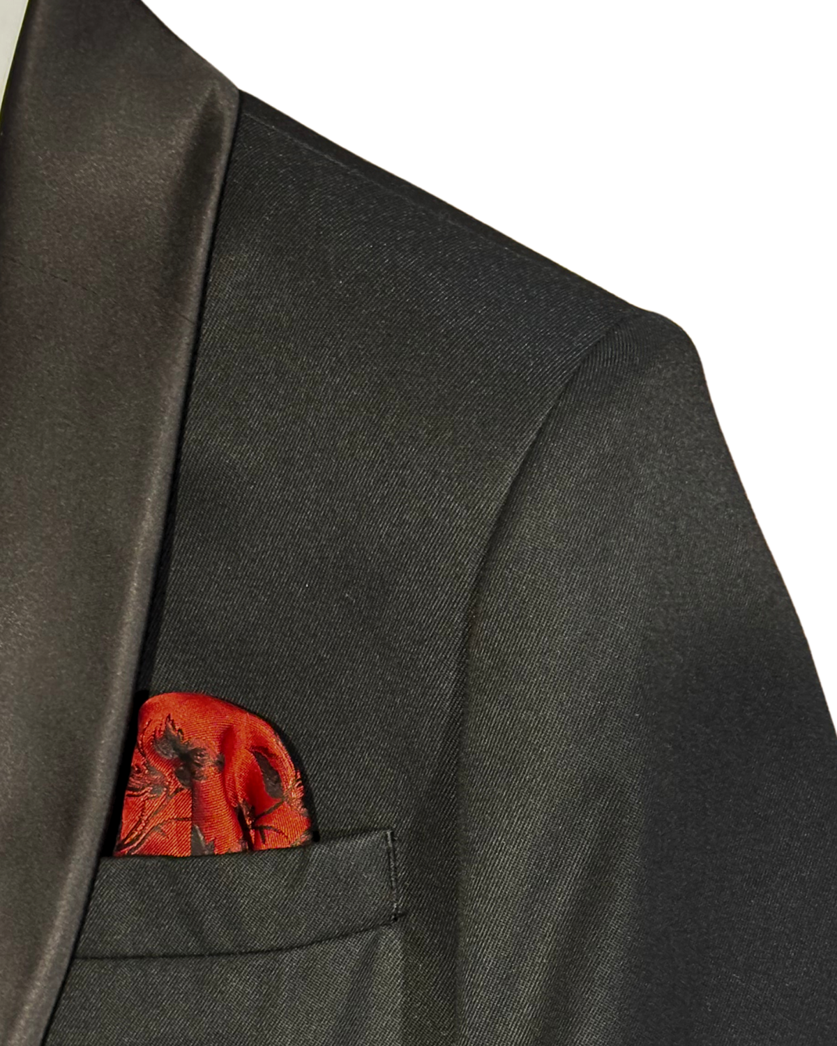 Close-up of a boys’ black tuxedo jacket showing the satin lapel, textured fabric and red patterned pocket square.
