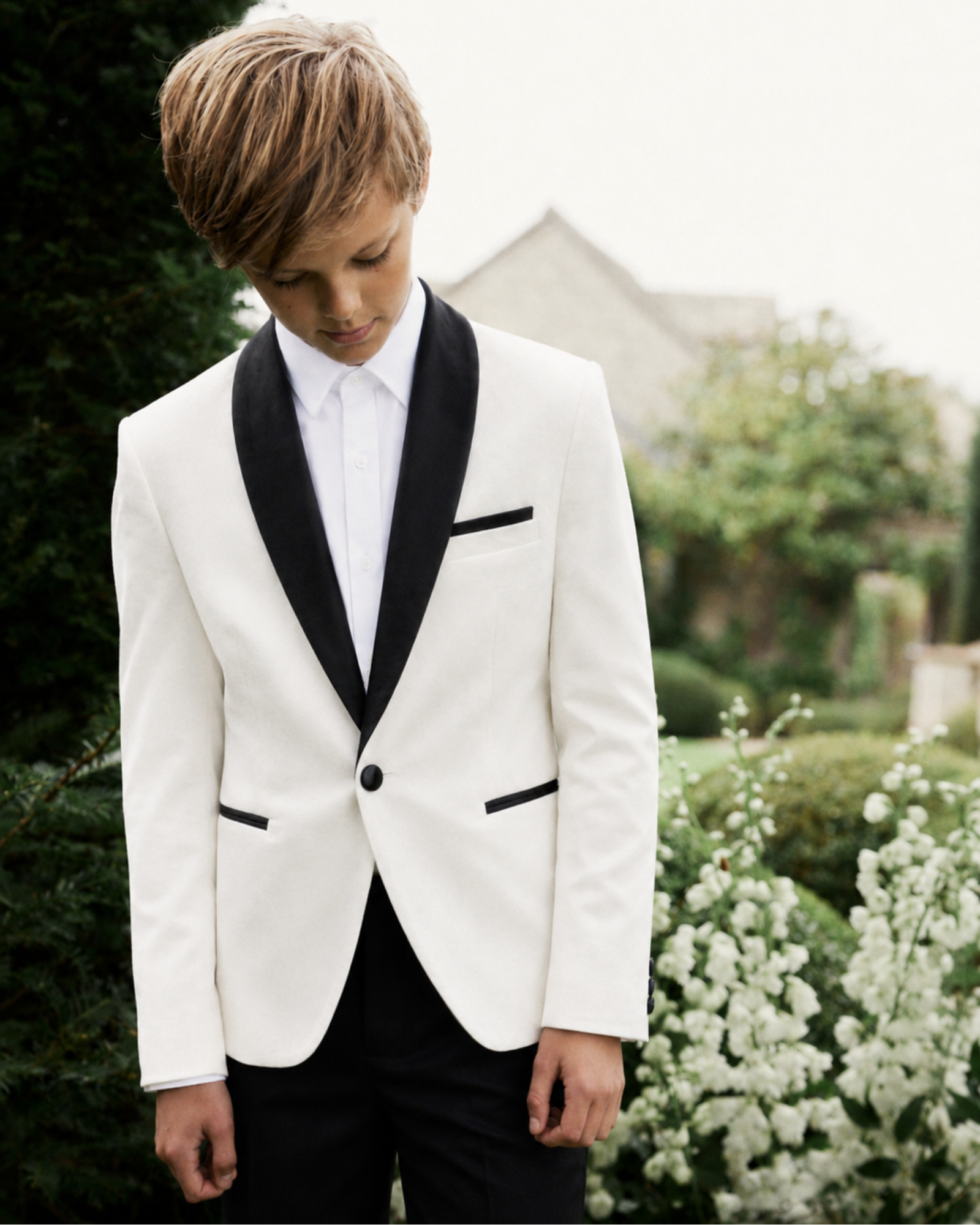 boy wearing a white tuxedo with black lapels in an outdoor setting.