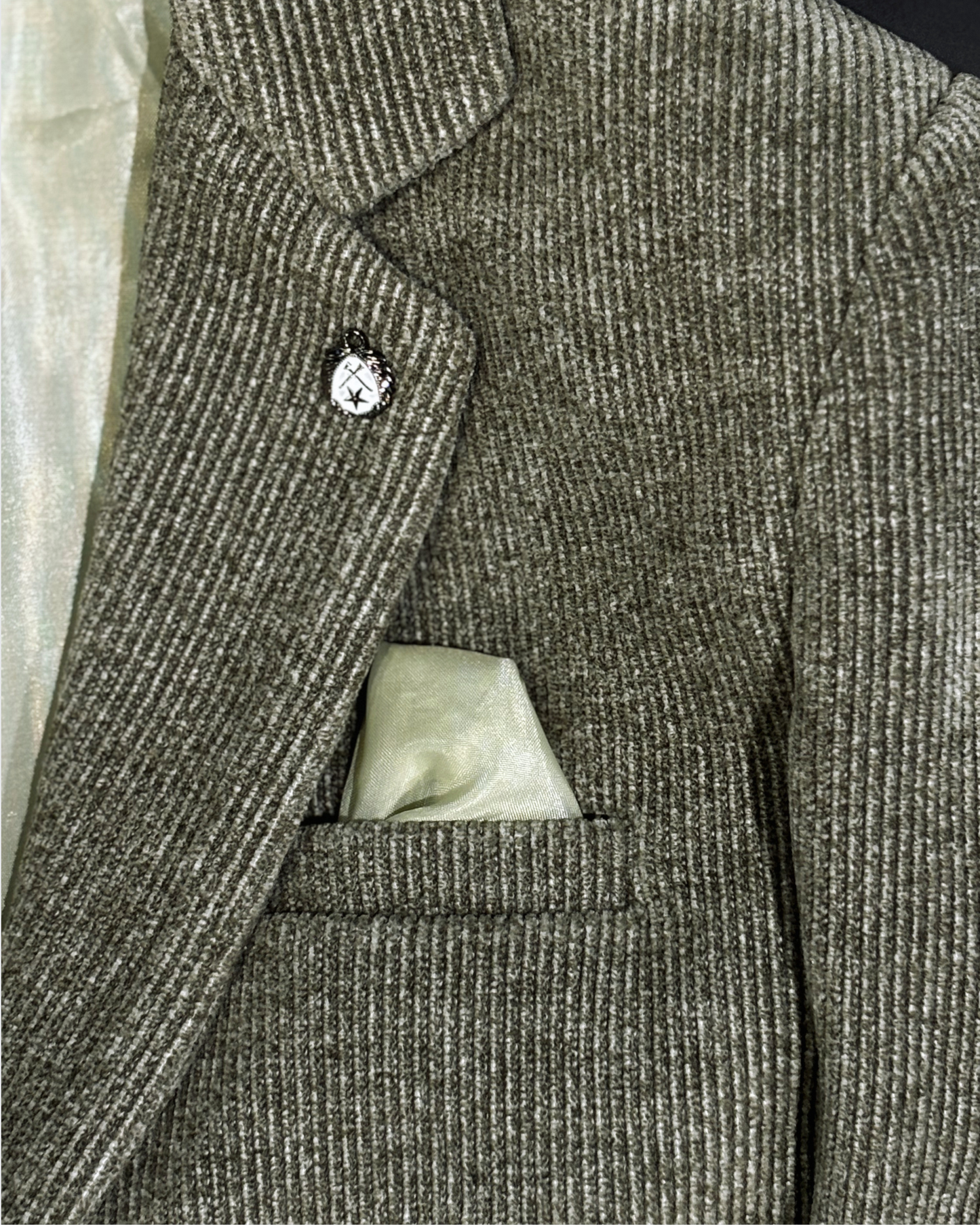 Close-up of olive corduroy blazer fabric showing textured ribbed pattern with built-in pocket square and lapel pin detail