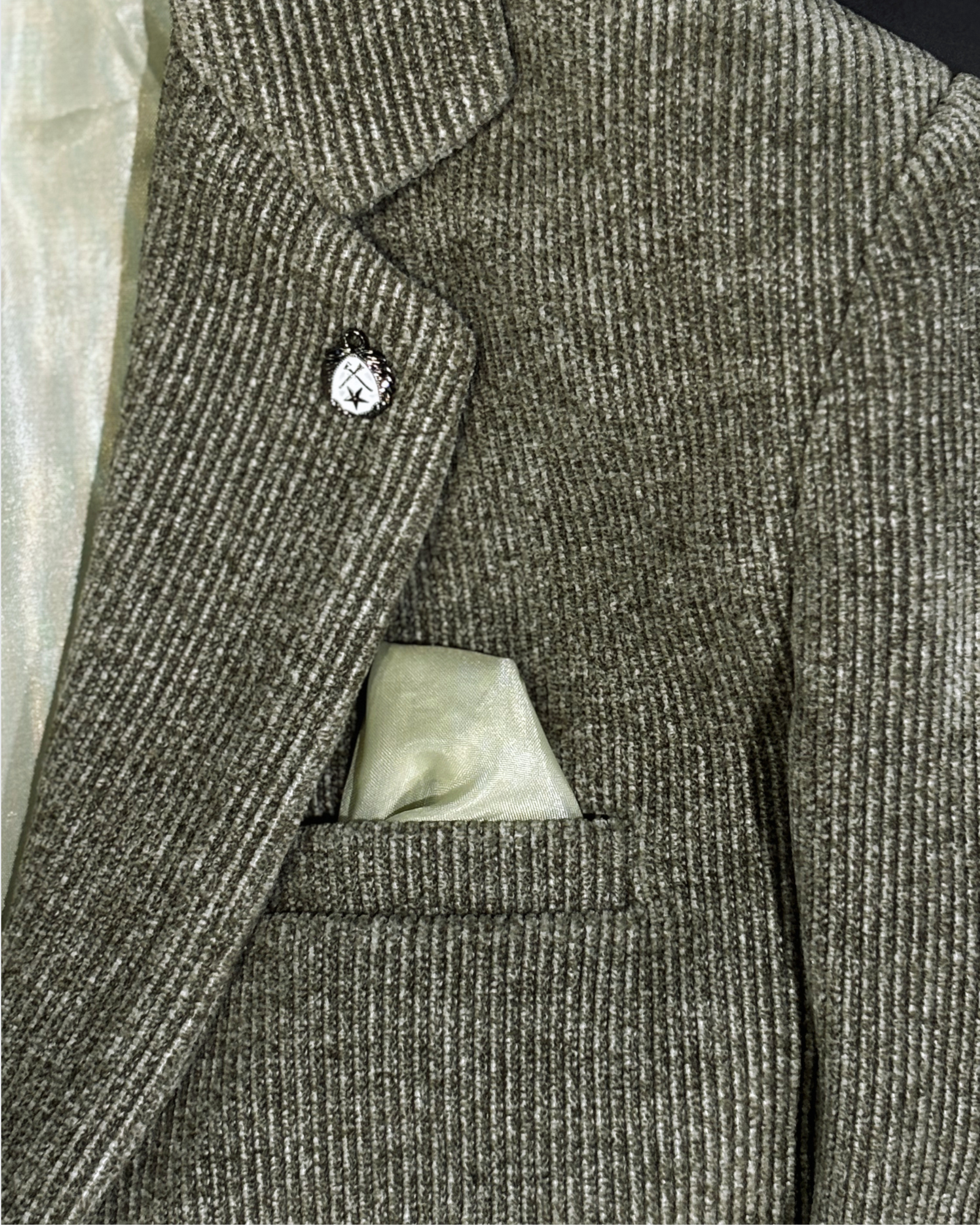 Close-up of olive corduroy blazer fabric showing textured ribbed pattern with built-in pocket square and lapel pin detail