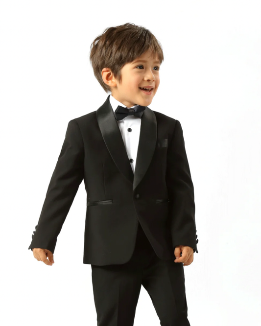 boy wearing black tux, including black shawl lapel blazer, white shirt, black dress pants, and black bow tie. he's facing the camera. 