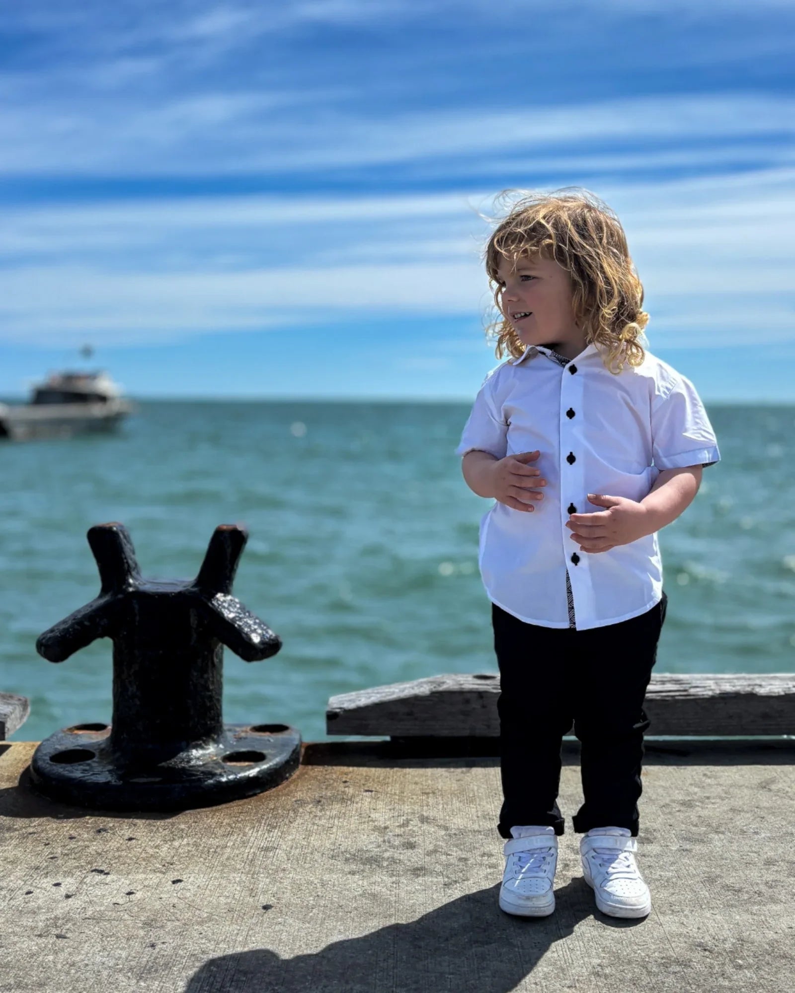 Boy wearing short sleeves shirt and chinos, standing on a pier, with water in the background