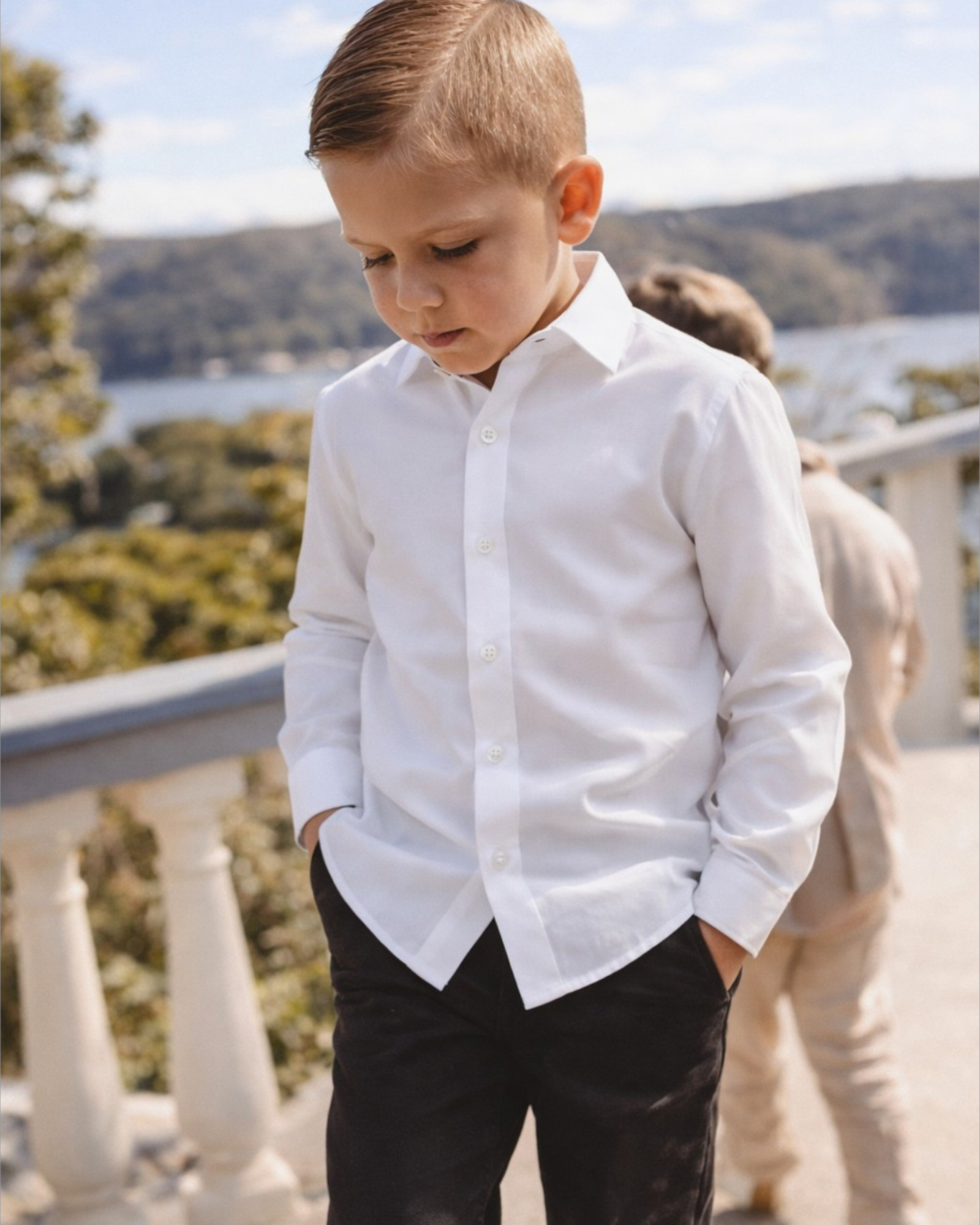 Young boy in a white shirt and black chinos standing outside on a balcony
