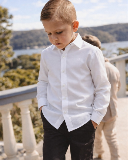 Young boy in a white shirt and black chinos standing outside on a balcony