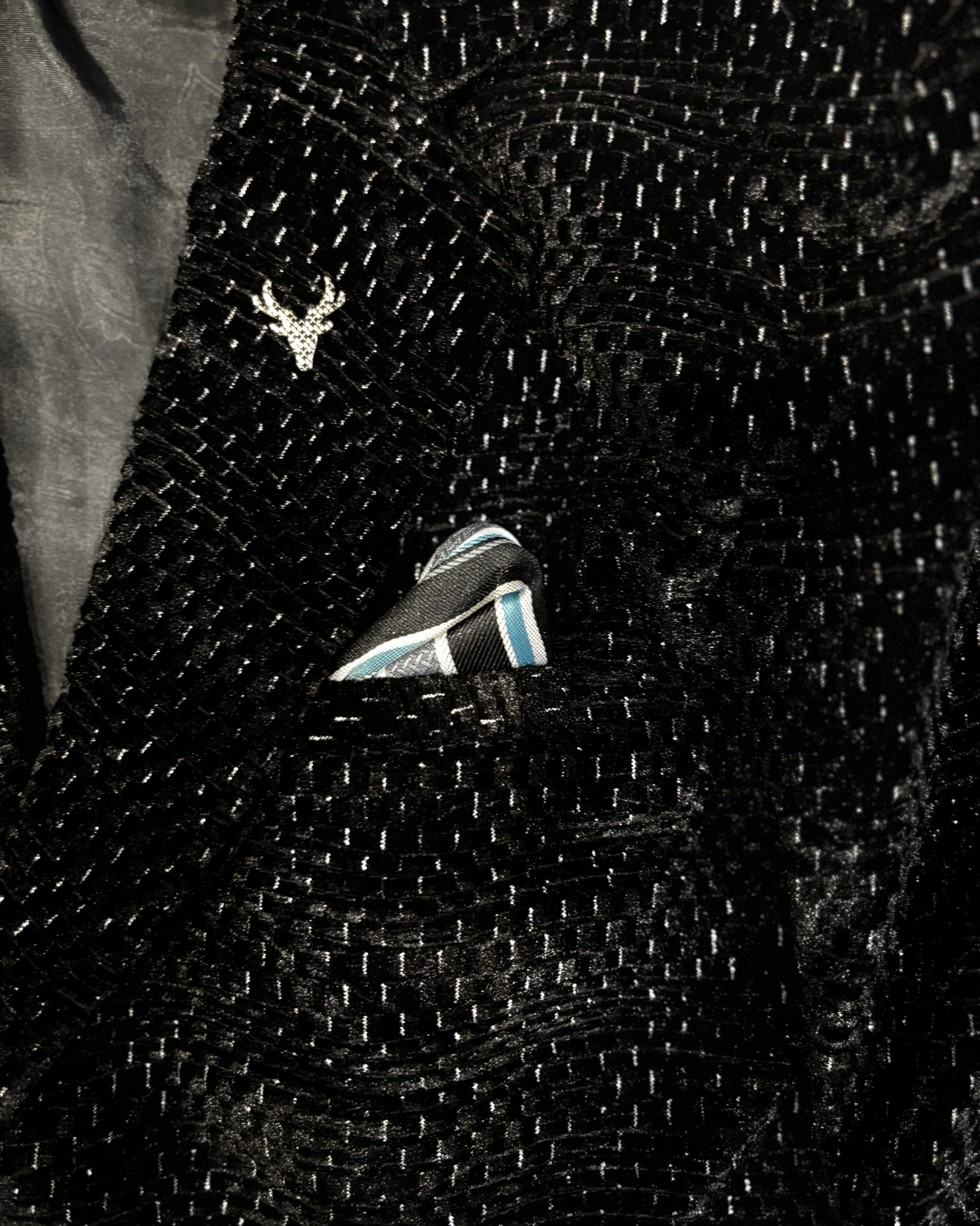 Close-up of boys black blazer textured jacquard fabric with pocket square and pin detail