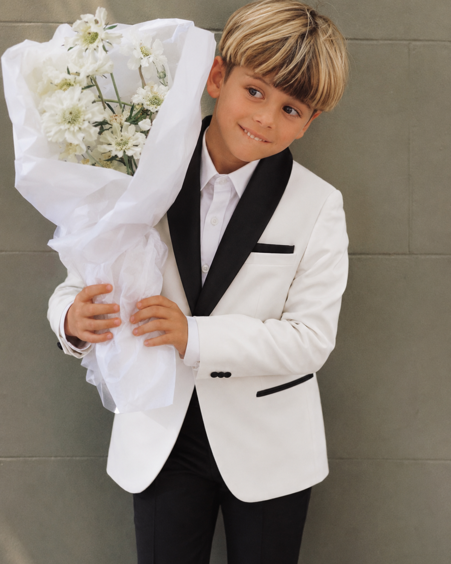 Young boy in a white velvet blazer holding a bouquet of white flowers 