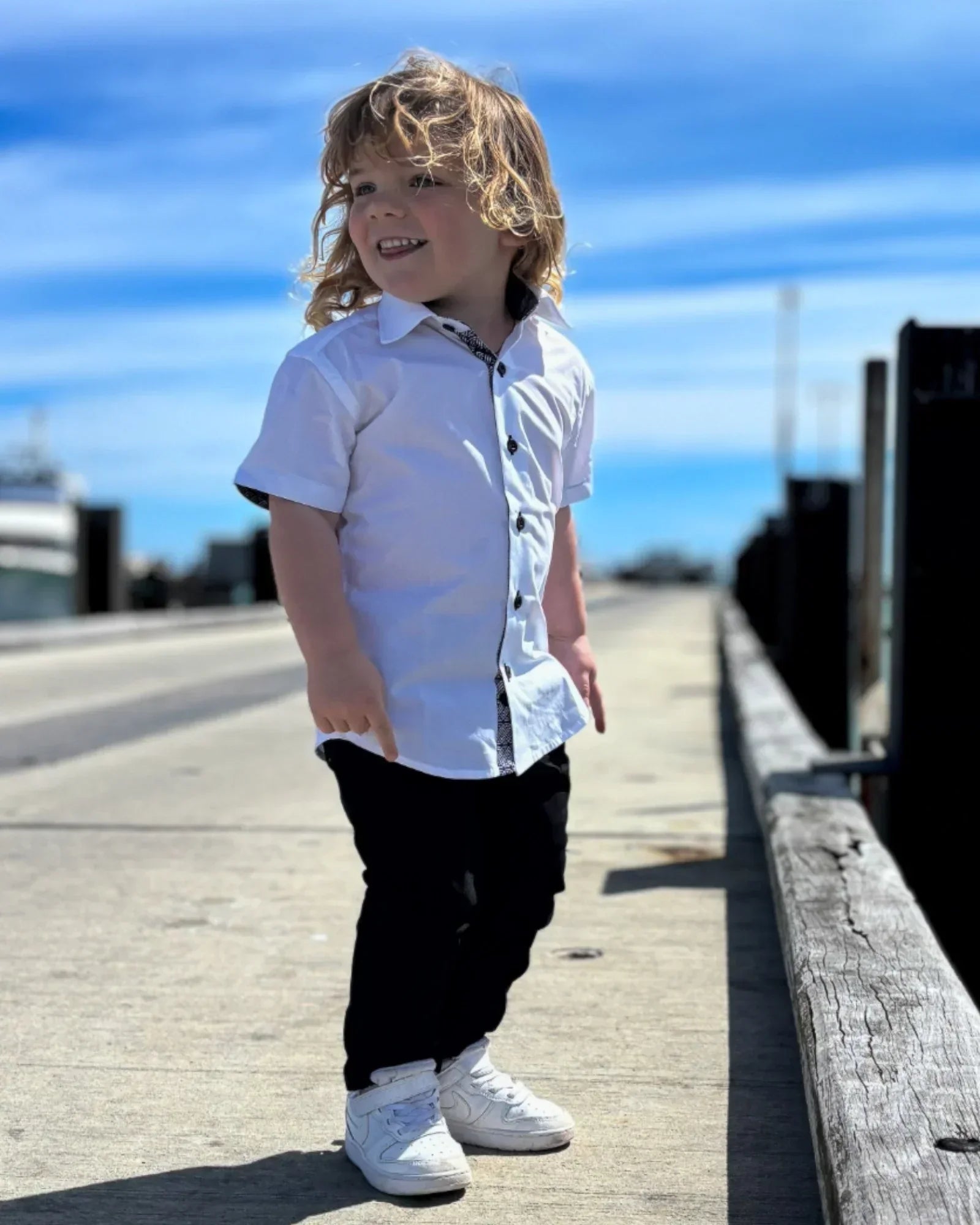 Boy wearing short sleeves shirt and chinos, standing on a pier