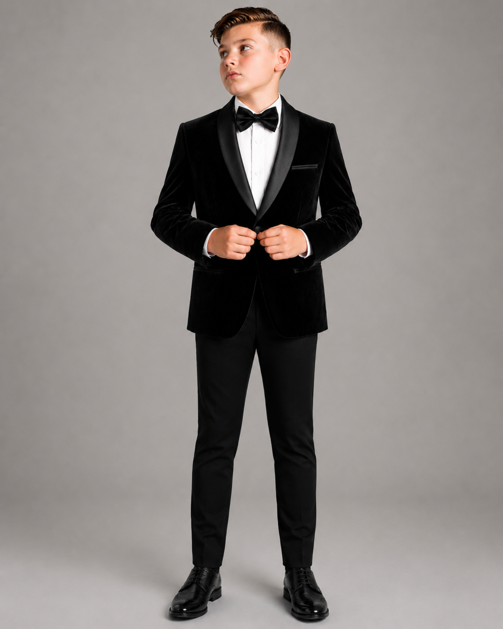 Young boy wearing a black tuxedo with a white shirt and black bow tie on a gray background
