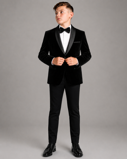 Young boy wearing a black tuxedo with a white shirt and black bow tie on a gray background