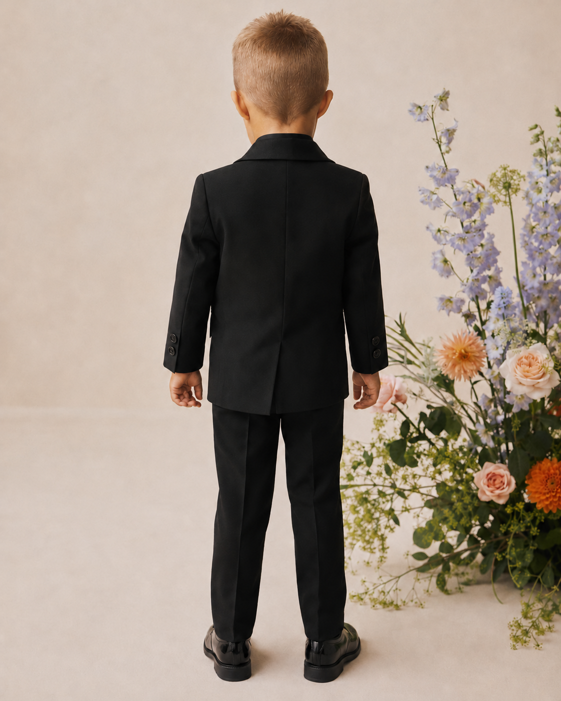 Child in a black tuxedo standing in front of a floral arrangement