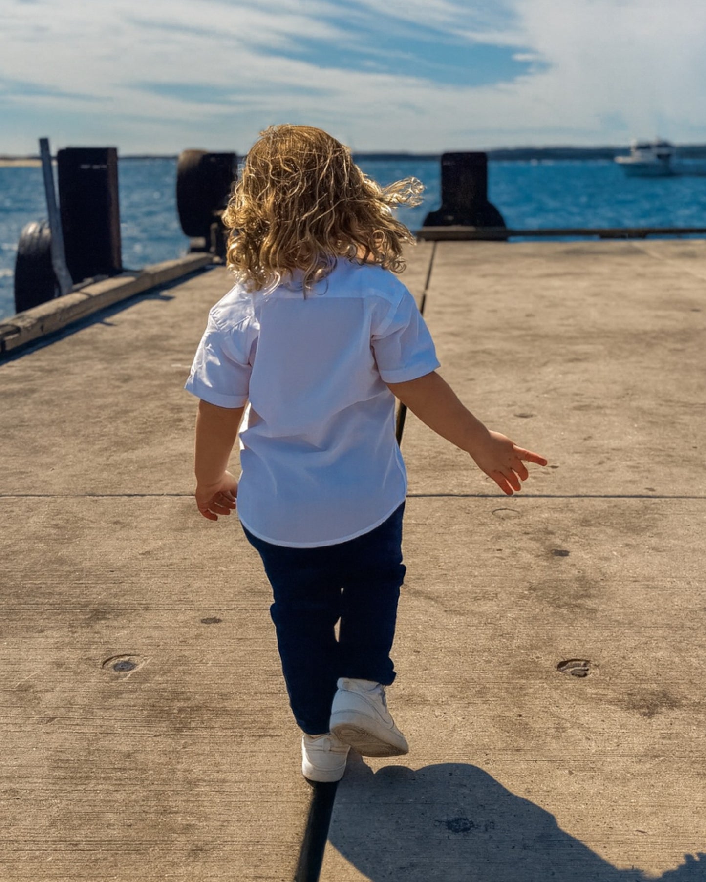 Boy wearing a white short sleeves shirt and black chinos walking on a pier.