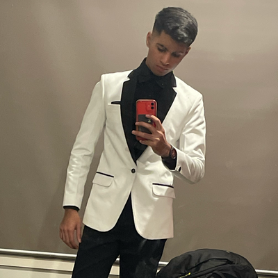A teenager takes a mirror selfie wearing a white velvet blazer over a black shirt, and wearing black trousers