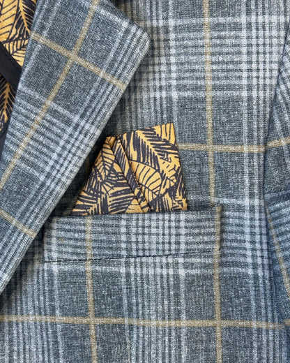Close-up of a blue and grey plaid blazer with yellow windowpane lines, featuring a folded yellow and navy patterned pocket square tucked into the chest pocket.