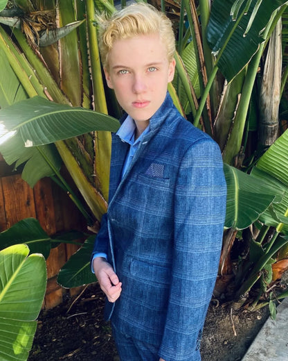 boy in a blue check/plaid blazer standing in front of palm trees. 