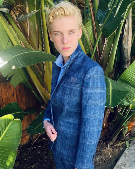 boy in a blue check/plaid blazer standing in front of palm trees. 