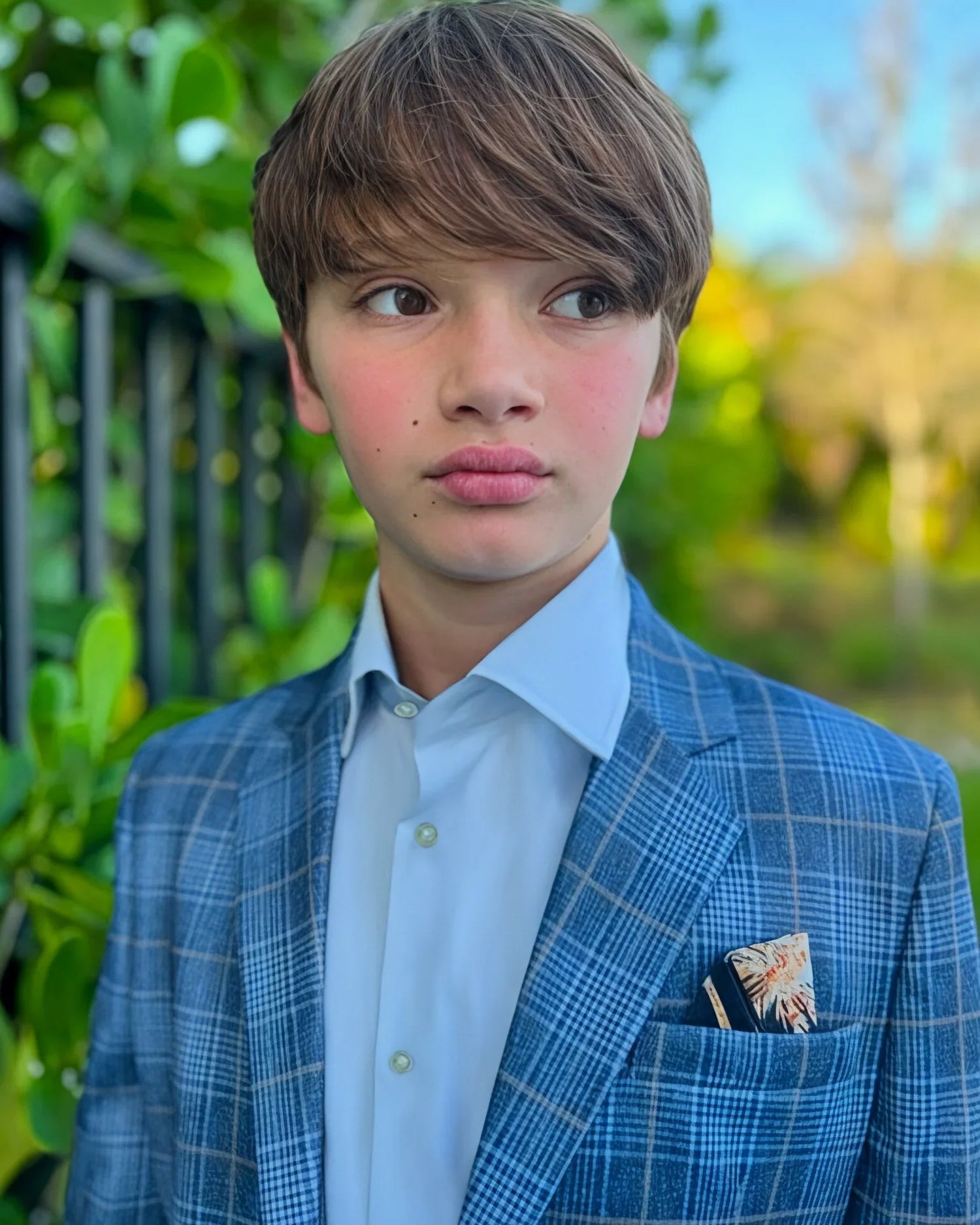 Young boy in a blue checkered suit with a pocket square, standing outdoors.