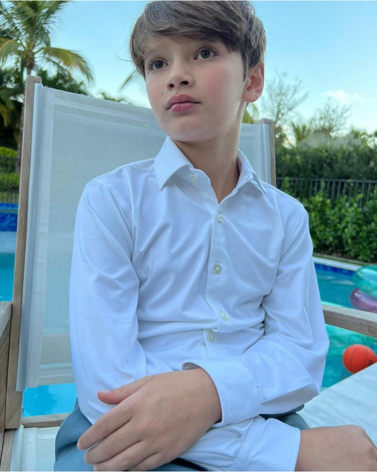 Child wearing a white shirt sitting by a pool with greenery in the background