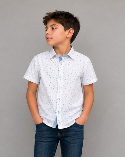 Young boy wearing a white patterned shirt and dark jeans against a gray background