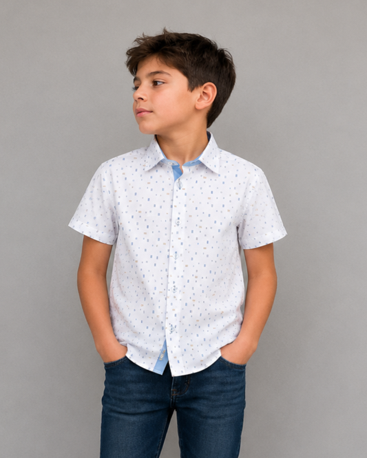 Young boy wearing a white patterned shirt and dark jeans against a gray background