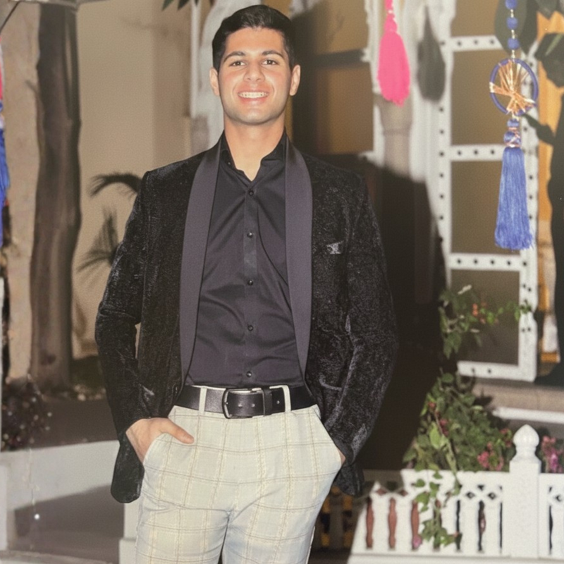 Man standing while wearing black velvet blazer, grey check pants and black shirt