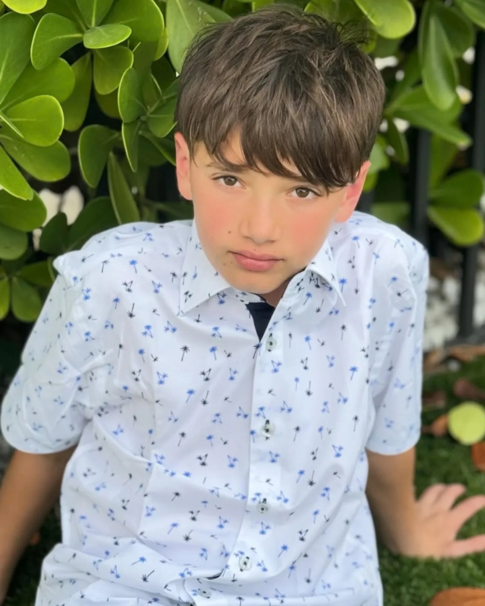 boy wearing Kids White Shirt With Palm Design sitting outside.